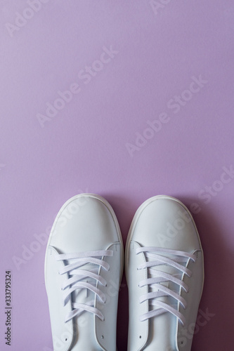 A pair of white sneakers on purple background. Copy space.