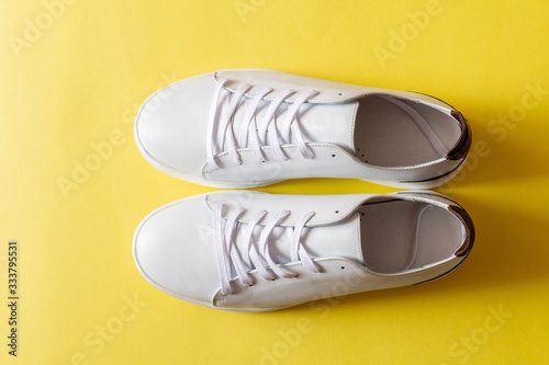 A pair of white leather sneakers on yellow background. Copy space.