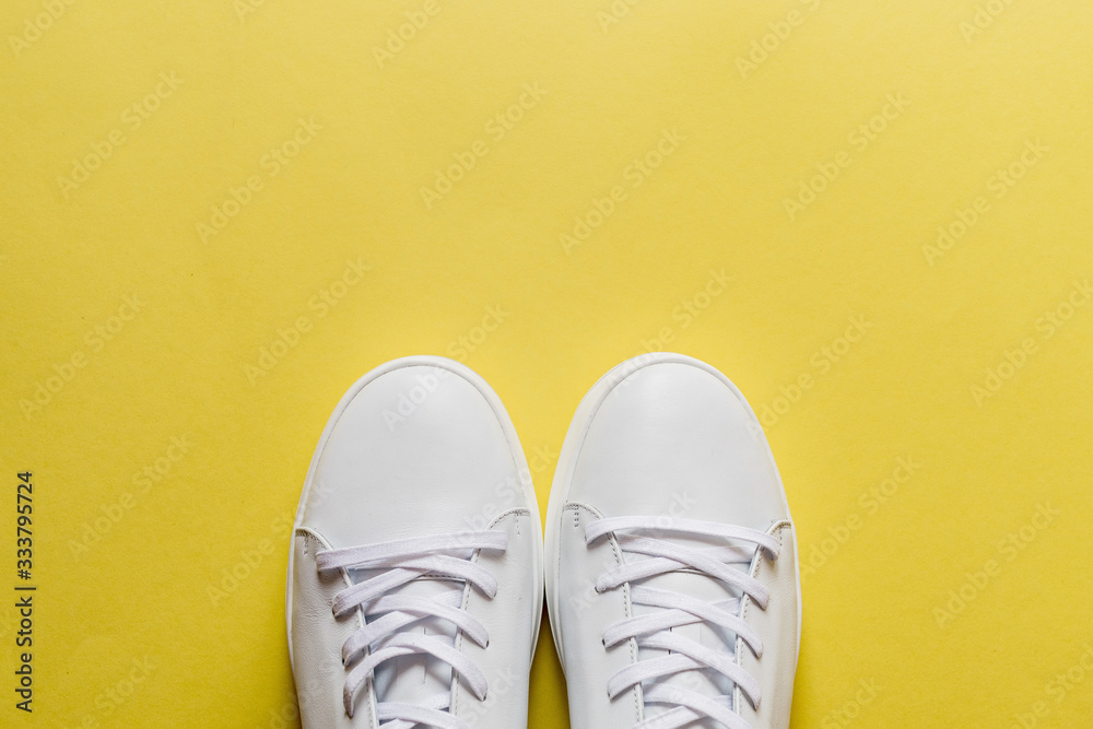 A pair of white leather sneakers on yellow background. Copy space. A pair of white leather sneakers on yellow background. Copy space.