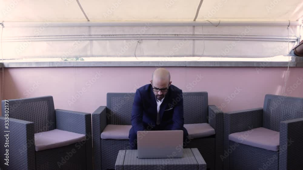 Stressed businessman in blue suit works on his laptop, on outdoor desk Stressed businessman in blue suit works on his laptop, on outdoor desk