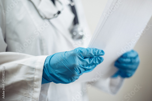 Closeup of a woman doctor wearing white medical gown and blue gloves, stethoscope. Female nurse holding papers with diagnosis for a patient. Coronavirus, covid-19 and sickness prevention concept.