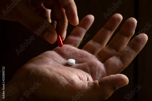 A man's hand holding a white pill. Hand holding a red capsule. on black background. Free space to write. Drug for legal use.