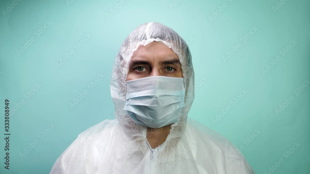 Man in protective suit, medical mask and gloves showing thumbs up on blue background Man in protective suit, medical mask and gloves showing thumbs up on blue background
