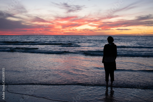 Silhouetted woman looks out over beach at sunset