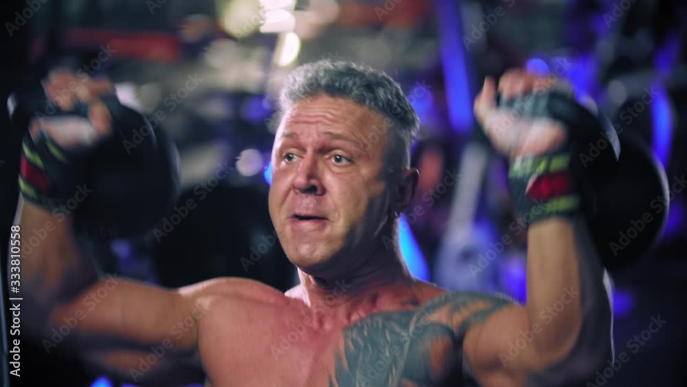 An adult man bodybuilder performing lifting heavy kettlebells putting effort An adult man bodybuilder performing lifting heavy kettlebells putting effort