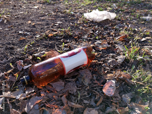 Close up dumped plastic beer bottle on the ground. Dry leaves. Enviromental pollution.