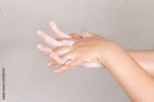 Young Woman  washing  hands with soap on  gray background.