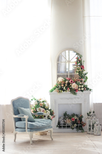 Bright room, fireplace and blue armchair. A lot of flowers and candles.