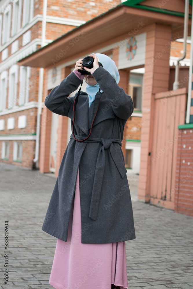 Muslim photographer in a blue shawl and in a pink dress photographs on a professional SLR camera