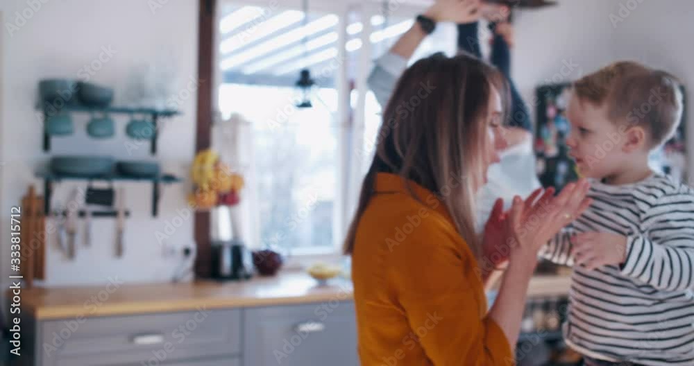 Happy young Caucasian mother and father playing with two little sons in the kitchen, family fun time at home slow motion Happy young Caucasian mother and father playing with two little sons in the kitchen, family fun time at home slow motion