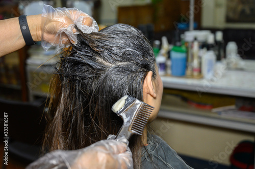 Cropped shot of a hairdresser hands doing colors a client's hair. Hair coloring process is to change to a color regarded as more fashionable or to restore the original hair color.