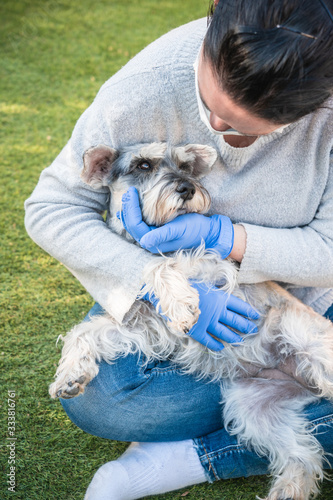 A woman protected with a mask and blue medical gloves hugs and caresses a dog