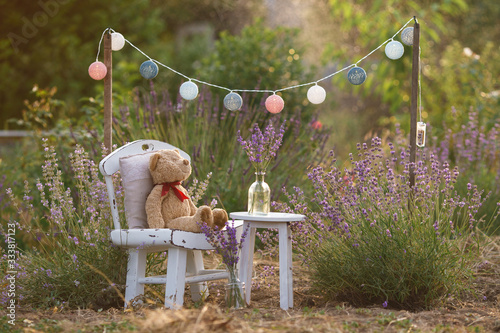 Children's photo zone on the lavender field. A battery-powered garland hangs over a white vintage chair and small table. Selective focus photo