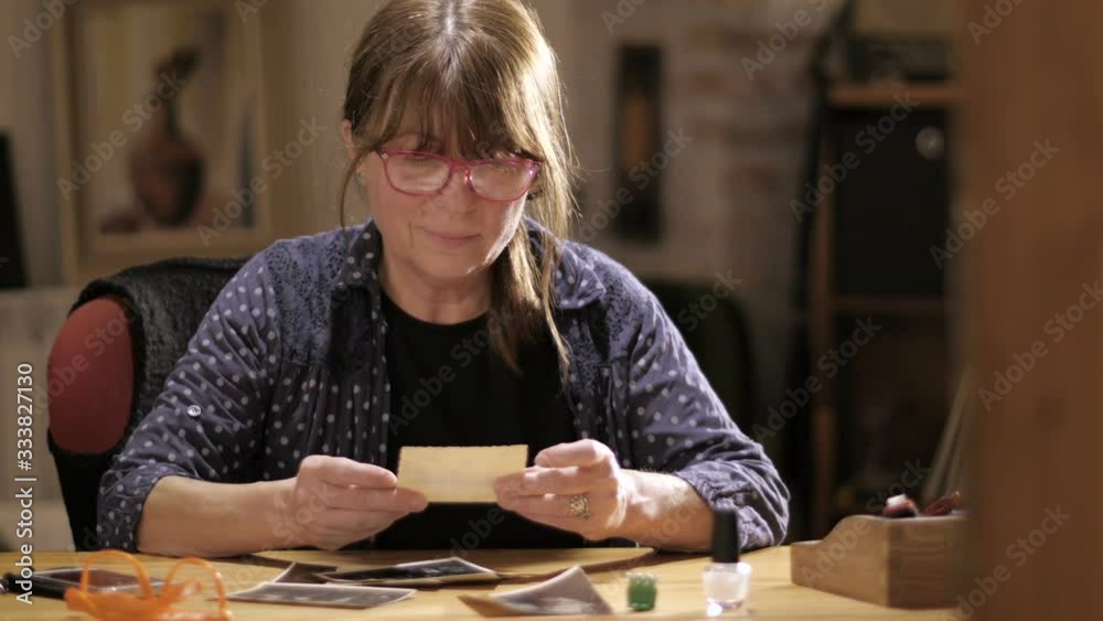 Mid age woman looks at old photos of family members Mid age woman looks at old photos of family members