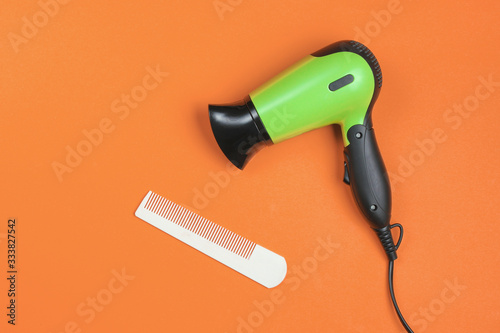 Minimalistic beauty and fashion still life. Hair dryer and comb on orange background. Top view, flat lay