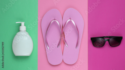 Beach accessories. Fashionable beach pink flip flops, sunblock bottle, sunglasses on colored paper background. Flat lay. Top view