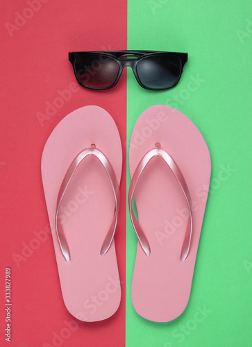 Summer still life. Beach accessories. Fashionable beach pink flip flops, sunglasses on pink green paper background. Flat lay. Top view
