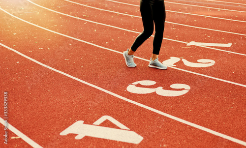 Young runner woman in sportwear run on stadium red track with numbers. Crop photo of female legs in leggings and sneakers
