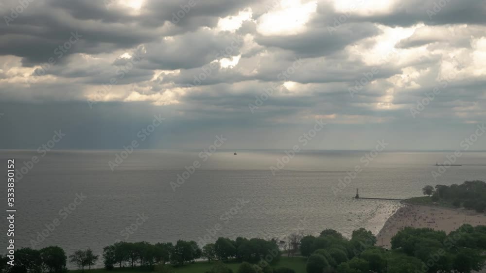 Aerial timelapse as people enjoy a warm summer day on the sand and in the water at the beach along Lake Michigan shoreline as clouds dance in the blue sky above. Aerial timelapse as people enjoy a warm summer day on the sand and in the water at the beach along Lake Michigan shoreline as clouds dance in the blue sky above.
