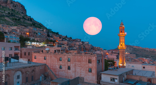 Sehidiye mosque with ful moon - Mardin old town at dusk. Historical beige colored limestone rock buildings 