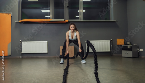 Young fit woman doing exercise with battle ropes in training class. Functional training  workout process.
