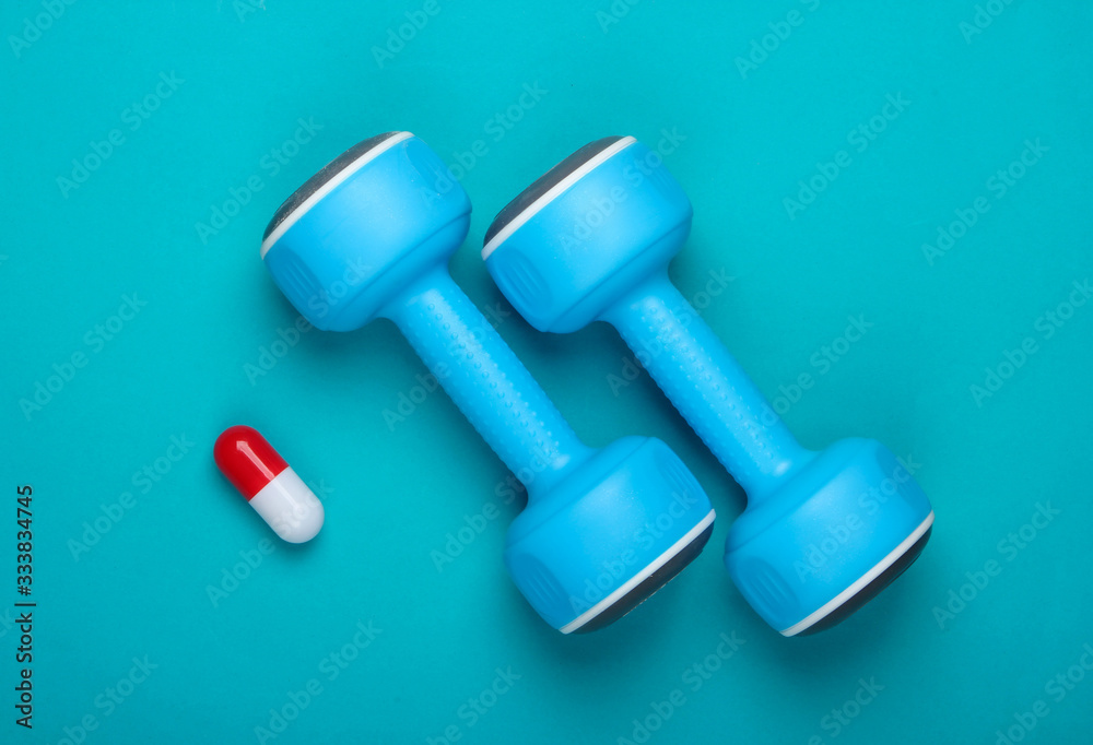 Pharmacology in sports. Dumbbell and capsule on blue background. Vitamins, steroids. Top view Pharmacology in sports. Dumbbell and capsule on blue background. Vitamins, steroids. Top view