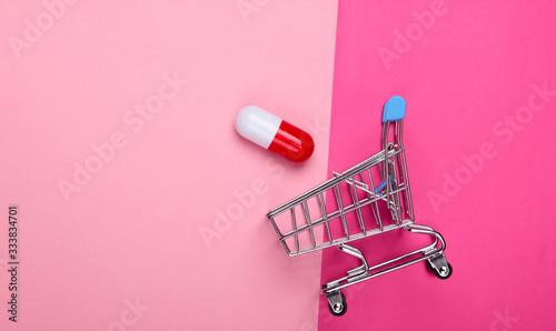 Mini shopping trolley, capsule tablet on pink background. Top view