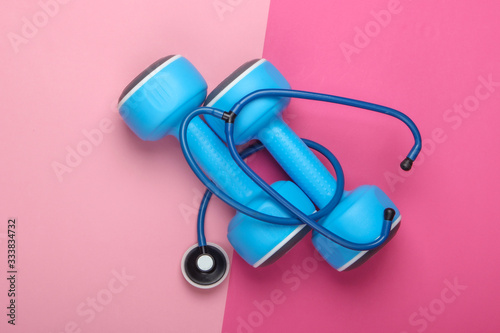 The concept of a healthy lifestyle and health care. Dumbbell with a stethoscope on a pink pastel background. Top view