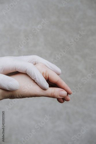 Two hands of a couple in plastic gloves holding each other. Virus protection concept, health issues, support, rescue life. Closeup aggainst gray wall, copyspace photo