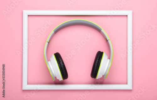 Stylish wireless stereo headphones on pink pastel background with white frame. Music lover. Gadgets. Top view.