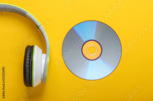 Half of stylish stereo headphones with cd disc on yellow background. Music lover. Retro 90s. Top view.