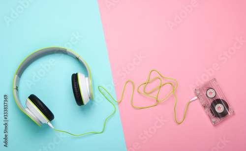 Stylish wired stereo headphones with audio cassette on pink blue pastel background. Music lover. Retro 80s. Top view.
