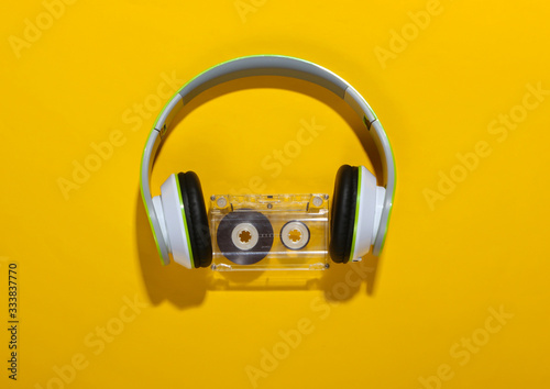 Stylish wireless stereo headphones and audio cassette on yellow background with shadow Fototapeta