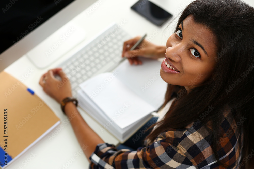 Black smiling woman sitting at workplace working with desktop pc studying or doing school homework concept Black smiling woman sitting at workplace working with desktop pc studying or doing school homework concept
