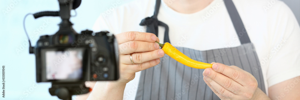 Smiling Vlogger Showing Hot Yellow Spicy Pepper. Professional Chef Recording Culinary Vlog on Camera at Home. Healthy Vegetable Ingredient in Male Hands. Organic Cayenne Horizontal Photography Smiling Vlogger Showing Hot Yellow Spicy Pepper. Professional Chef Recording Culinary Vlog on Camera at Home. Healthy Vegetable Ingredient in Male Hands. Organic Cayenne Horizontal Photography