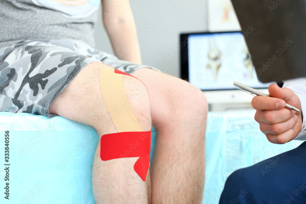 Close-up of patient with red patches bound on aching leg joint sitting in therapist's clinic office. Smart doctor checking damaged ankle. Medical treatment concept