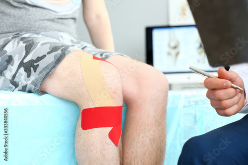 Close-up of patient with red patches bound on aching leg joint sitting in therapist's clinic office. Smart doctor checking damaged ankle. Medical treatment concept