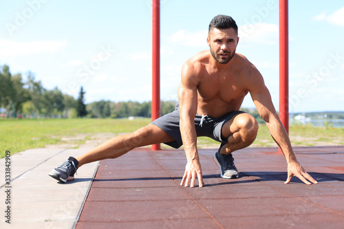 Sporty man doing workout stretching exercises for legs outdoors