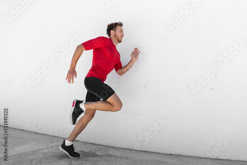 Running man jogging fast profile sideways against white wall outdoor background. Male athlete training healthy active lifestyle.