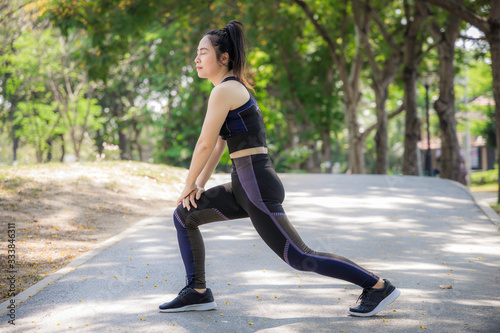 Portrait rear of an Asian woman wearing a black sports bra and she is body warm up for a workout by running in the park. Urban health care concept.