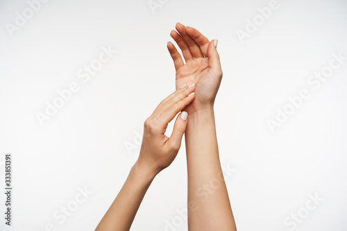 Close-up of pretty lady's hands touching gentle each others while posing over white background, keeping hands raised while lathering hands