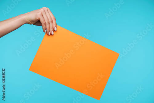 Young secretary with white manicure keeping her hand raised while holding orange envelope with important documents while standing over blue background