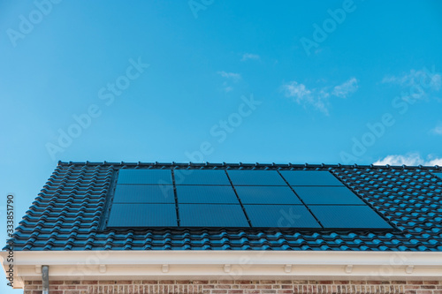 Newly build house in the Netherlands with solar panels attached on the roof against a sunny sky Close up of new building black solar panels