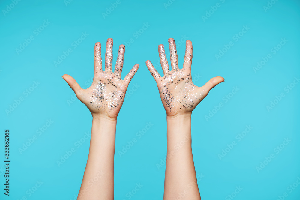 Pretty woman's hands with silver sparkles keeping all fingers separately while showing palms at camera, isolated against blue background. Human hands and gesturing Pretty woman's hands with silver sparkles keeping all fingers separately while showing palms at camera, isolated against blue background. Human hands and gesturing