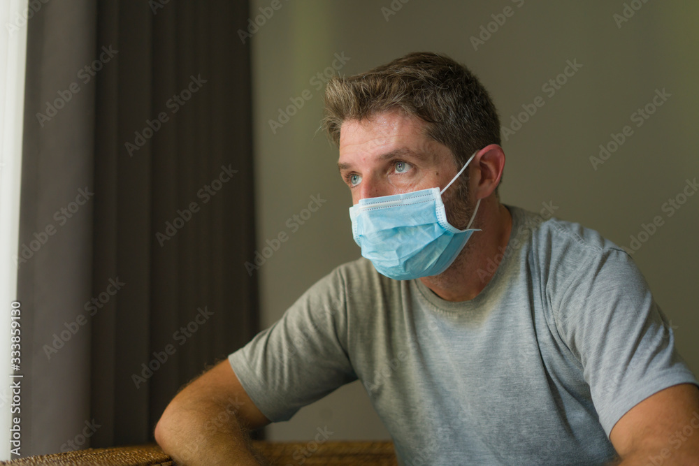 covid-19 virus lockdown - sad and worried man in medical mask thinking and feeling scared in quarantine following stay at home instructions to contain virus pandemic