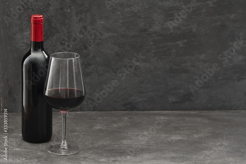 Red wine bottle and wine glass on dark concrete background with copy space. Wine making and wine degustation concept.