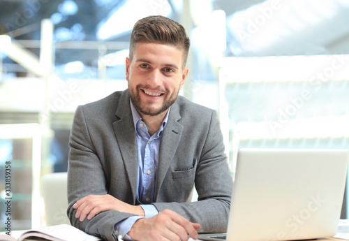 Portrait of happy businessman sitting at office desk, looking at camera, smiling.