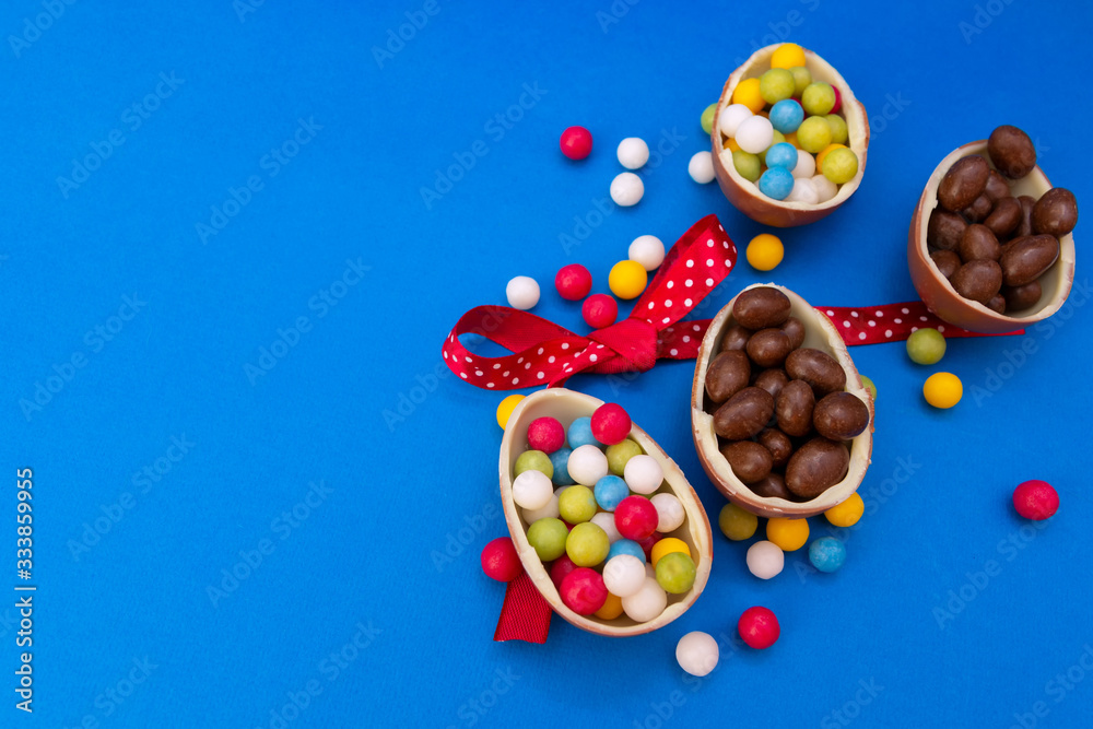 Chocolate easter eggs with bonbon and ribbon on blue background with copy space