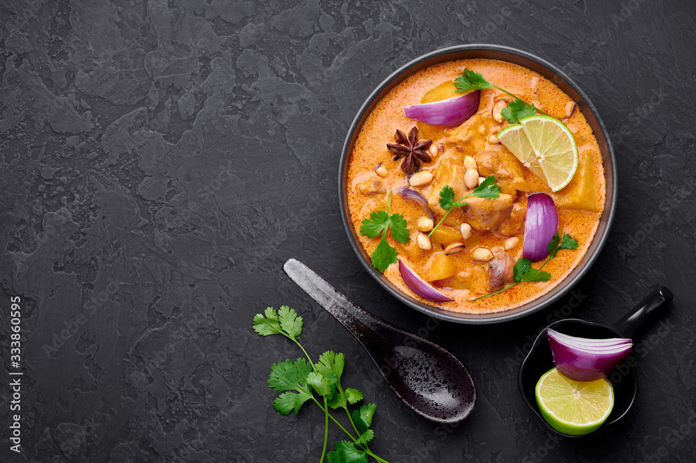 A Chicken Massaman Curry in black bowl at dark slate background. Massaman Curry is Thai Cuisine dish with chicken meat, potato, onion and many spices. Thai Food. Copy space. Top view - obrazy, fototapety, plakaty 
