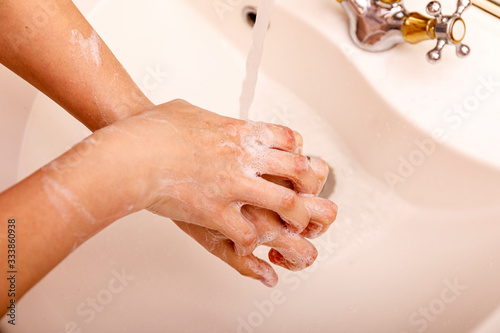 Young woman washing hands in modern sink with soap and lathering suds to protect against the coronavirus or covid 19. Bathroom hygiene concept.